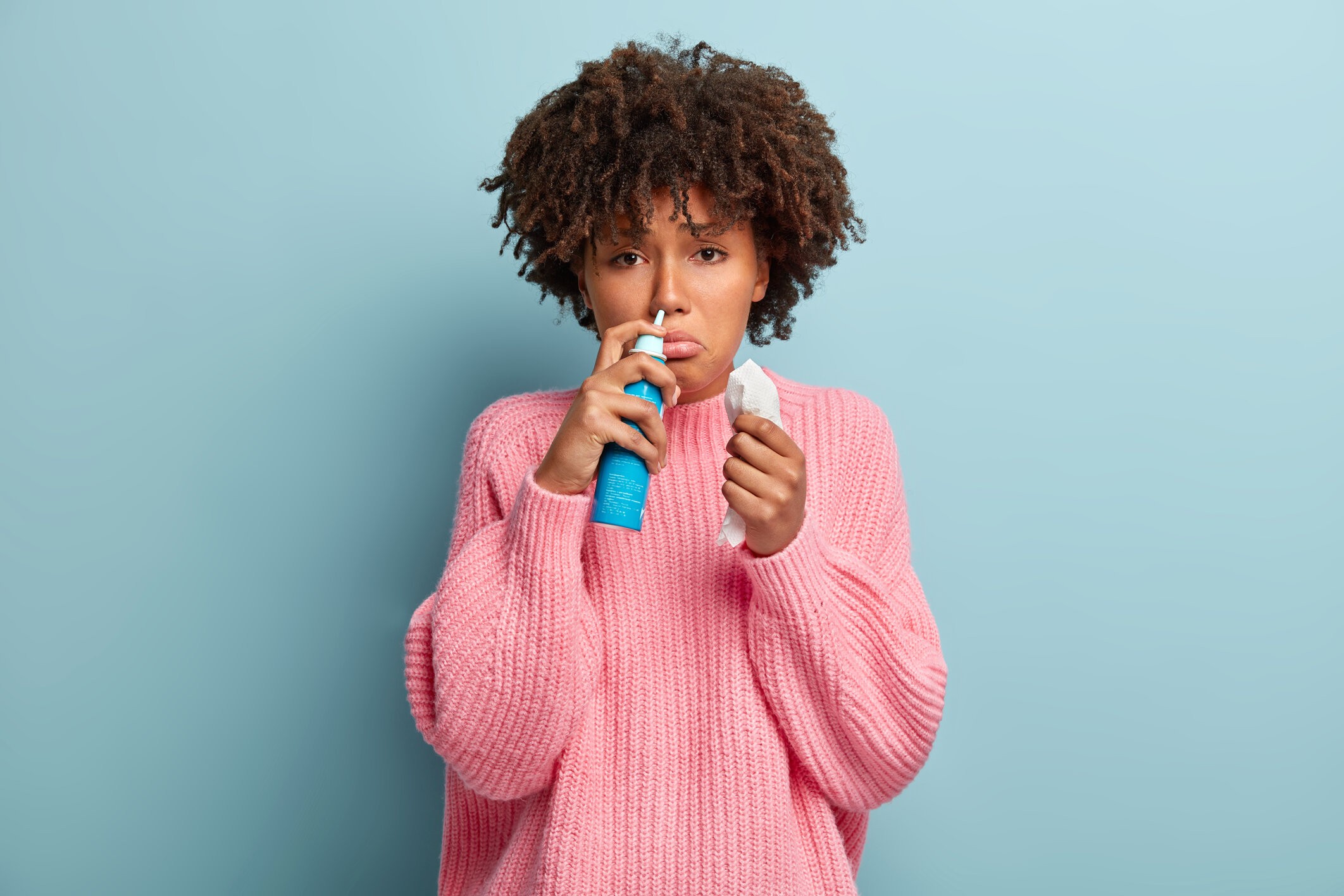 rsz portrait displeased afro american woman sniffs nasal aerosol feels sick has running nose uses medication blocked nose holds tissue has sad facial expression wears pink jumper