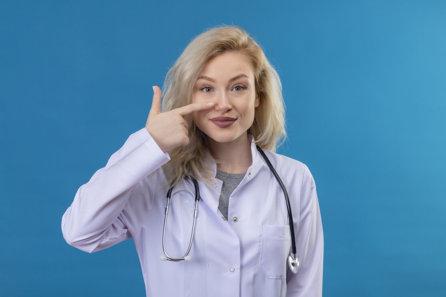 rsz smiling young doctor wearing stethoscope medical gown points nose blue wall